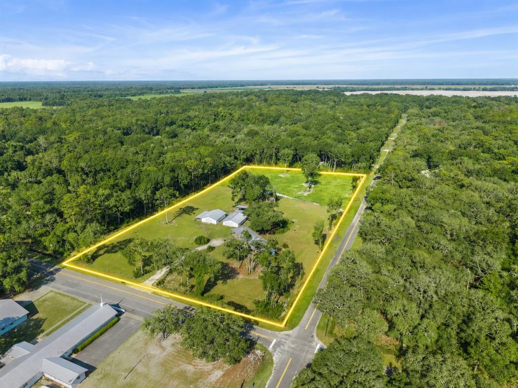 An aerial view shows a house and outbuildings on a large, grassy, tree-lined lot — 12450 NW 85TH AVENUE, CHIEFLAND, FL