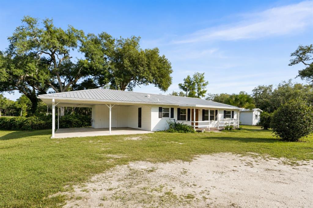 A white single-story house with a metal roof and an attached carport sits on grass — 12450 NW 85TH AVENUE, CHIEFLAND, FL