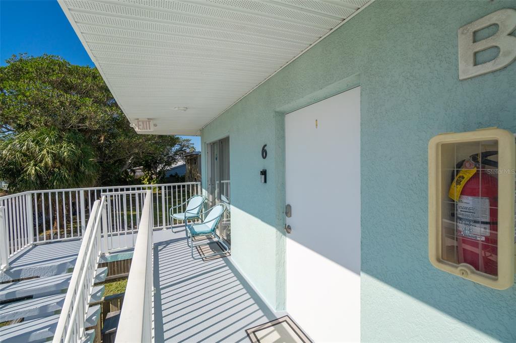 An exterior walkway with a white door, two chairs, and a fire extinguisher cabinet — 425 HARRISON AVENUE UNIT 6-2, CAPE CANAVERAL, FL