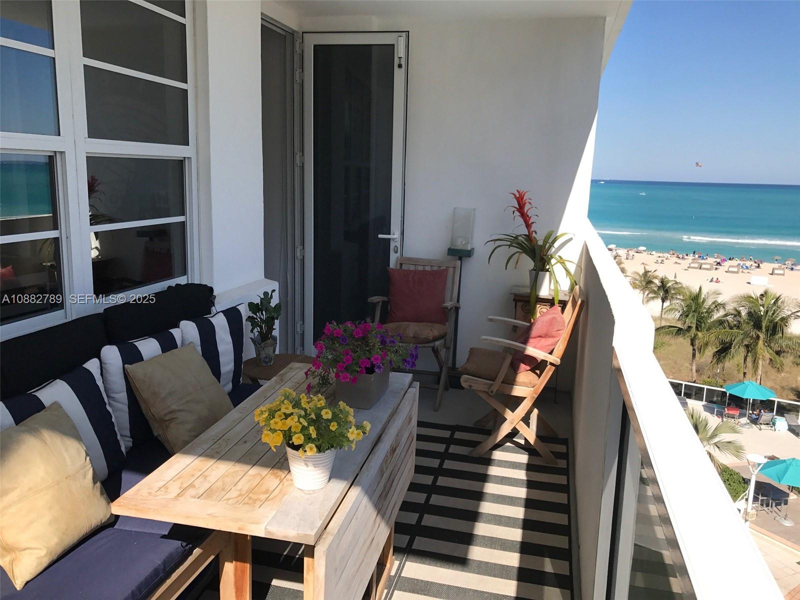 A balcony with outdoor seating, a wooden table, and potted plants overlooks a sandy beach — 100 Lincoln Rd # 644, Miami Beach FL 33139, MIAMI BEACH, FL
