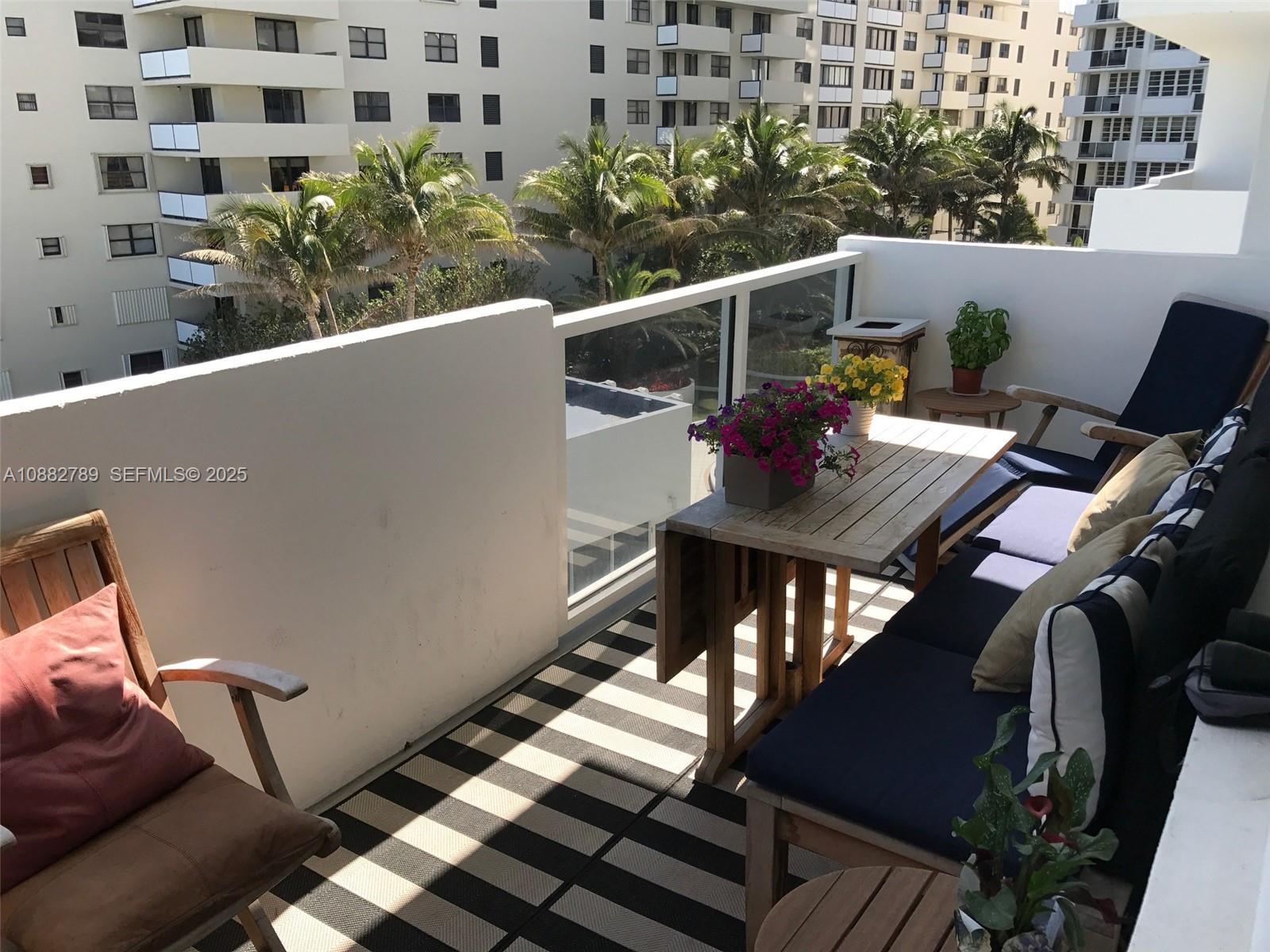 A balcony features a wooden table, bench seating with cushions, and a striped outdoor rug — 100 Lincoln Rd # 644, Miami Beach FL 33139, MIAMI BEACH, FL