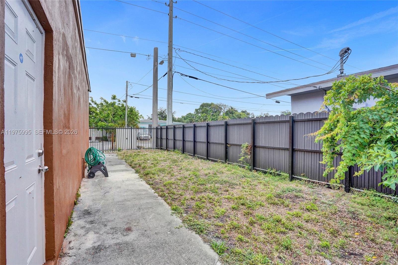 A concrete walkway runs alongside a brown building wall next to a fenced yard — 5595 NW 17th Ave, Miami FL 33142, MIAMI, FL
