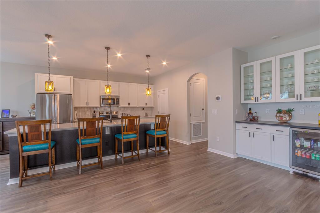 A kitchen features white cabinetry, a dark island with four stools, and a beverage refrigerator — 1261 LONE PALM WAY, ST CLOUD, FL