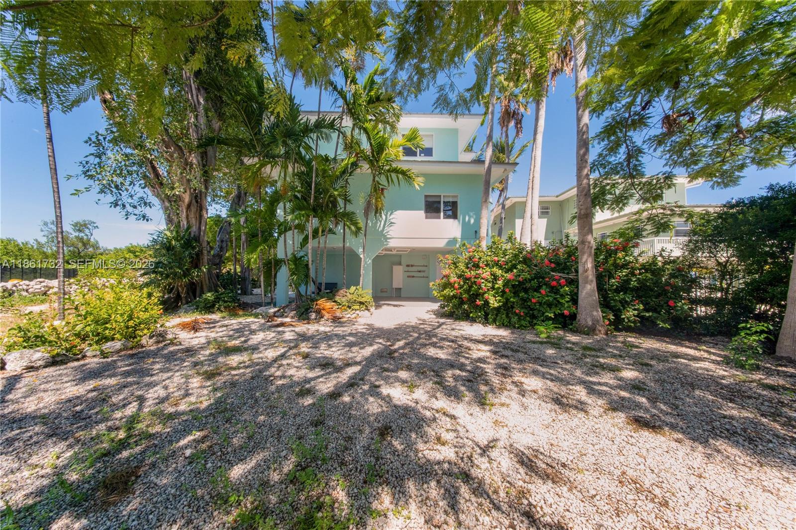 A light green, elevated house stands behind a gravel driveway surrounded by palm trees — 316 N Dr, Islamorada FL 33036, ISLAMORADA, FL