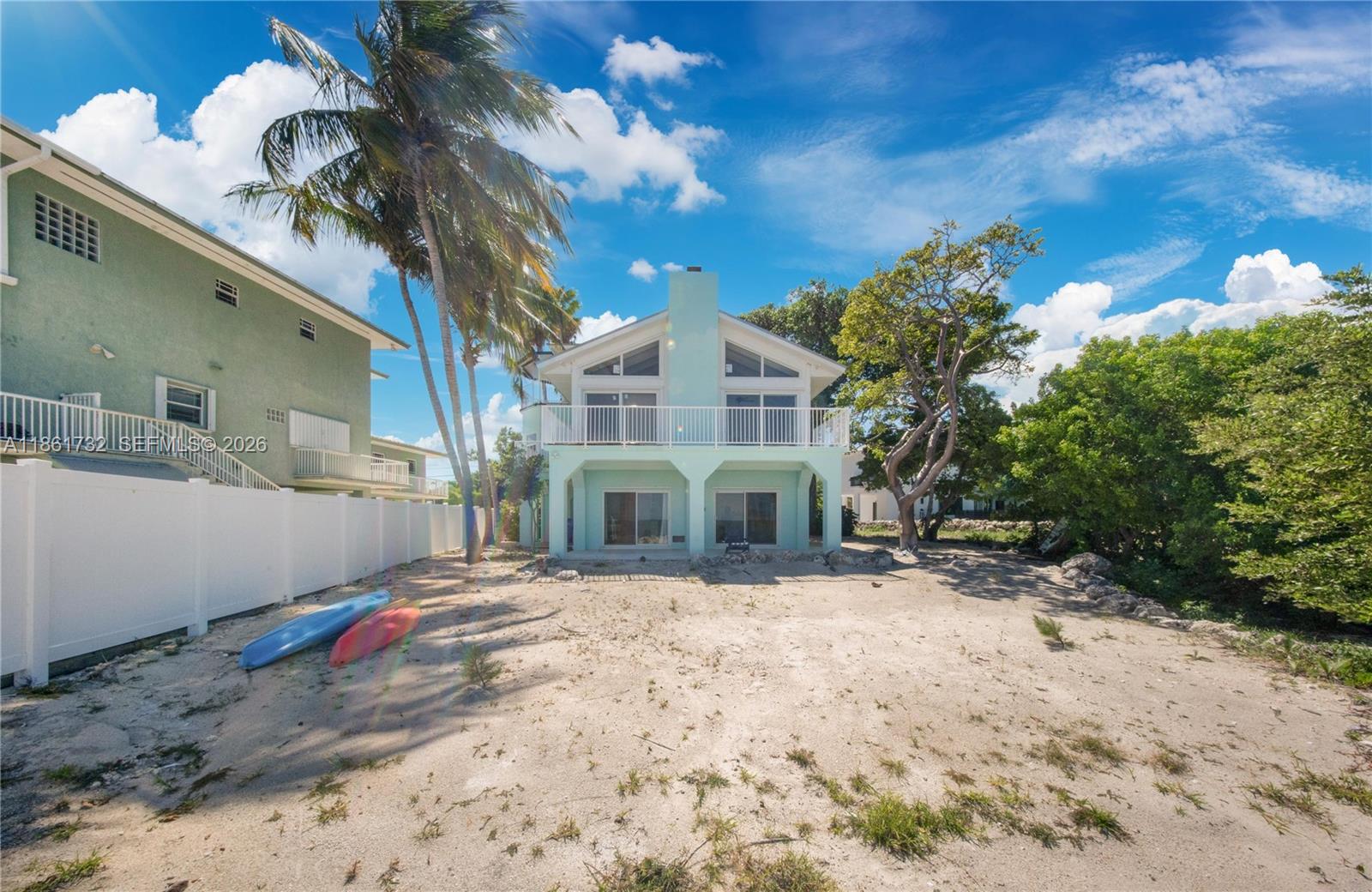 A light green two-story house with a balcony stands on a sandy lot with kayaks — 316 N Dr, Islamorada FL 33036, ISLAMORADA, FL