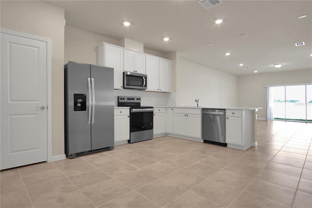 A kitchen with white cabinets, stainless steel appliances, and tile flooring in an open space — 4292 CHESTER SPRINGS BOULEVARD, DAVENPORT, FL