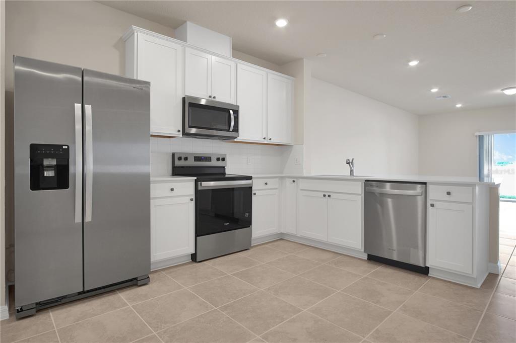 A kitchen features white cabinets, stainless steel appliances, and light-colored tile flooring — 4292 CHESTER SPRINGS BOULEVARD, DAVENPORT, FL