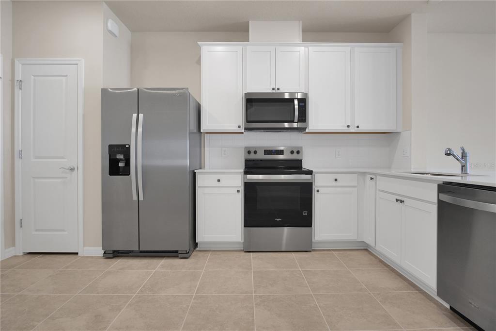 A kitchen features white cabinets, stainless steel appliances, and light-colored tile flooring — 4292 CHESTER SPRINGS BOULEVARD, DAVENPORT, FL