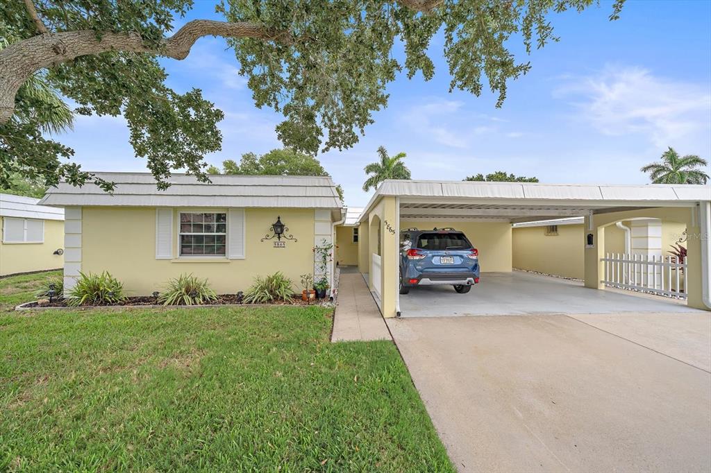 A yellow single-story house features a concrete driveway and an attached carport with a vehicle — 5865 TIDEWOOD AVENUE UNIT 8, SARASOTA, FL