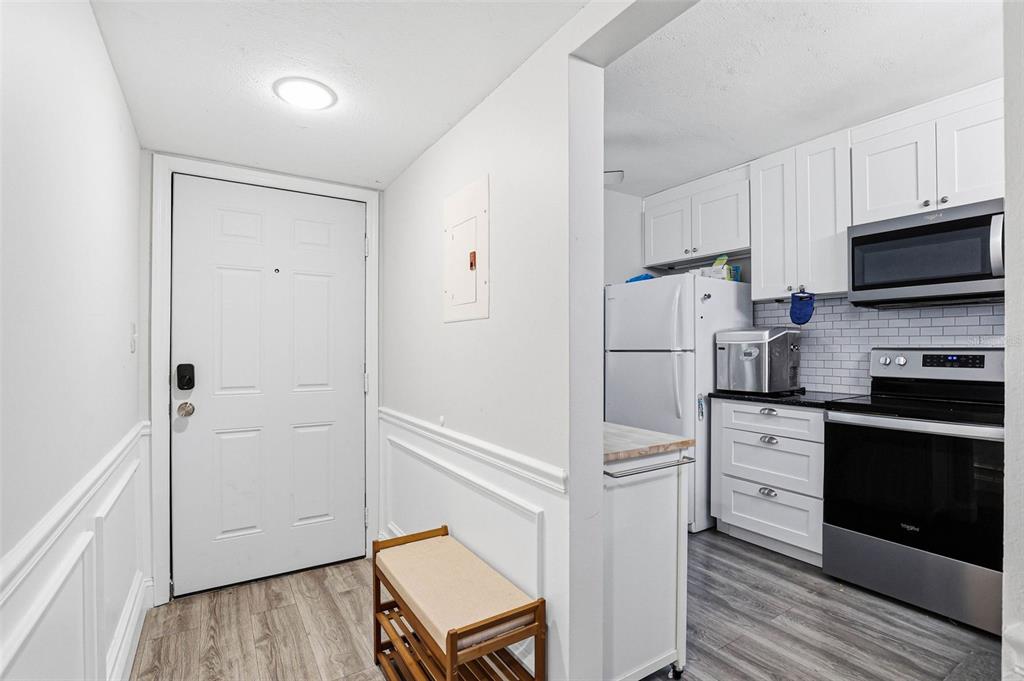 A white front door opens into a hallway with a bench beside a small kitchen — 2424 W TAMPA BAY BOULEVARD UNIT M404, TAMPA, FL
