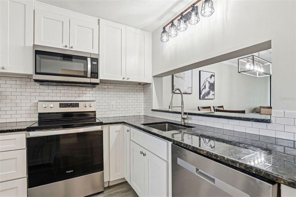 A kitchen features white cabinets, stainless steel appliances, black granite countertops, and a subway tile backsplash — 2424 W TAMPA BAY BOULEVARD UNIT M404, TAMPA, FL