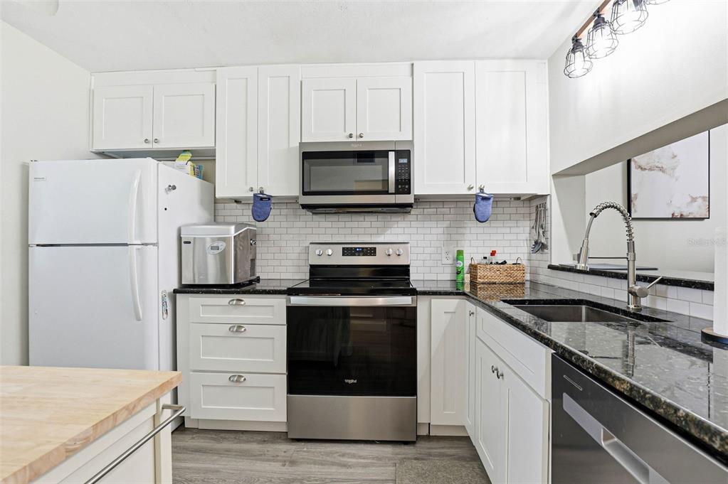 A kitchen features white cabinets, stainless steel appliances, dark countertops, and a subway tile backsplash — 2424 W TAMPA BAY BOULEVARD UNIT M404, TAMPA, FL