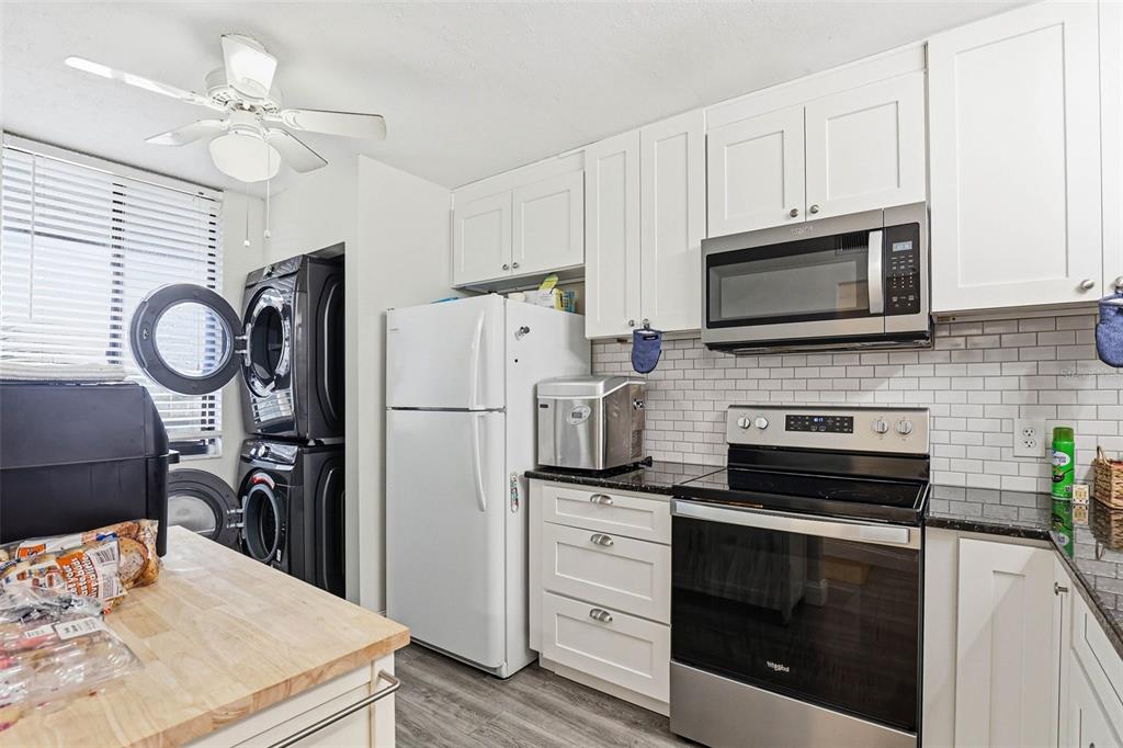 A kitchen features white cabinetry, stainless steel appliances, a subway tile backsplash, and stacked laundry — 2424 W TAMPA BAY BOULEVARD UNIT M404, TAMPA, FL