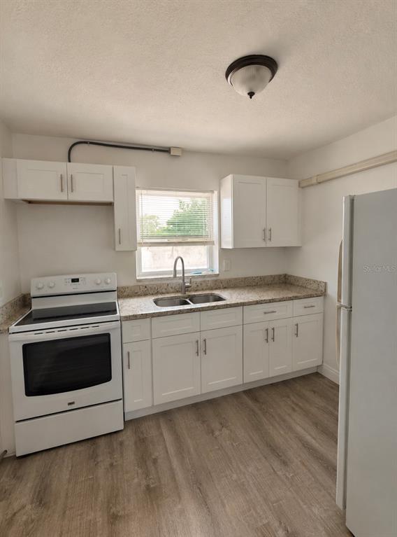 A kitchen features white cabinets, granite countertops, a white stove, and wood-look flooring — 1407 N BETTY LANE UNIT 4, CLEARWATER, FL