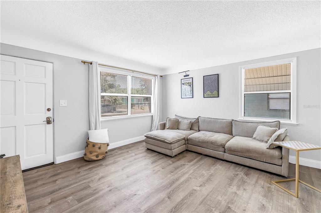 A living room features light gray walls, wood-look flooring, a large sectional sofa, and two windows — 4729 12TH AVENUE S, ST PETERSBURG, FL