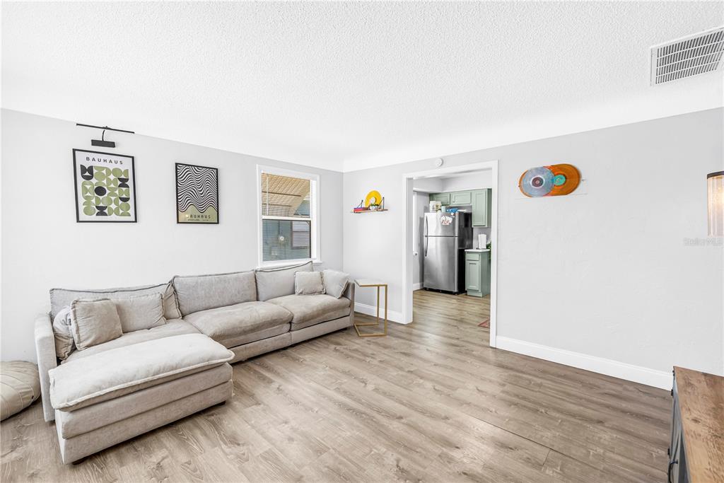 A living room with a gray sectional sofa, wood-look flooring, and a doorway to a kitchen — 4729 12TH AVENUE S, ST PETERSBURG, FL