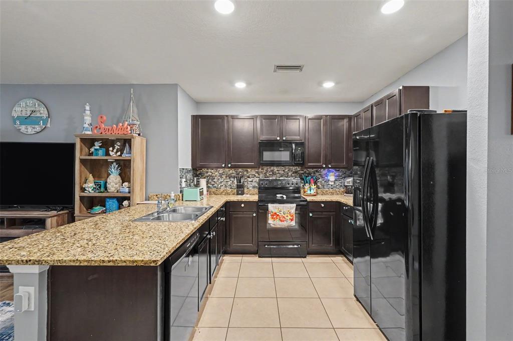 A kitchen features dark wood cabinets, granite countertops, black appliances, and a tiled floor — 3918 WILLOW HAMMOCK DRIVE, PALMETTO, FL