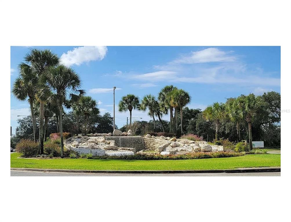 A stone waterfall feature sits in the center of a landscaped roundabout with palm trees — 216 MARION OAKS BOULEVARD SW UNIT 8, OCALA, FL