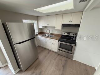 A kitchen features stainless steel appliances, white cabinets, a brown countertop, and light wood flooring — 3009 S MANHATTAN AVENUE UNIT B, TAMPA, FL