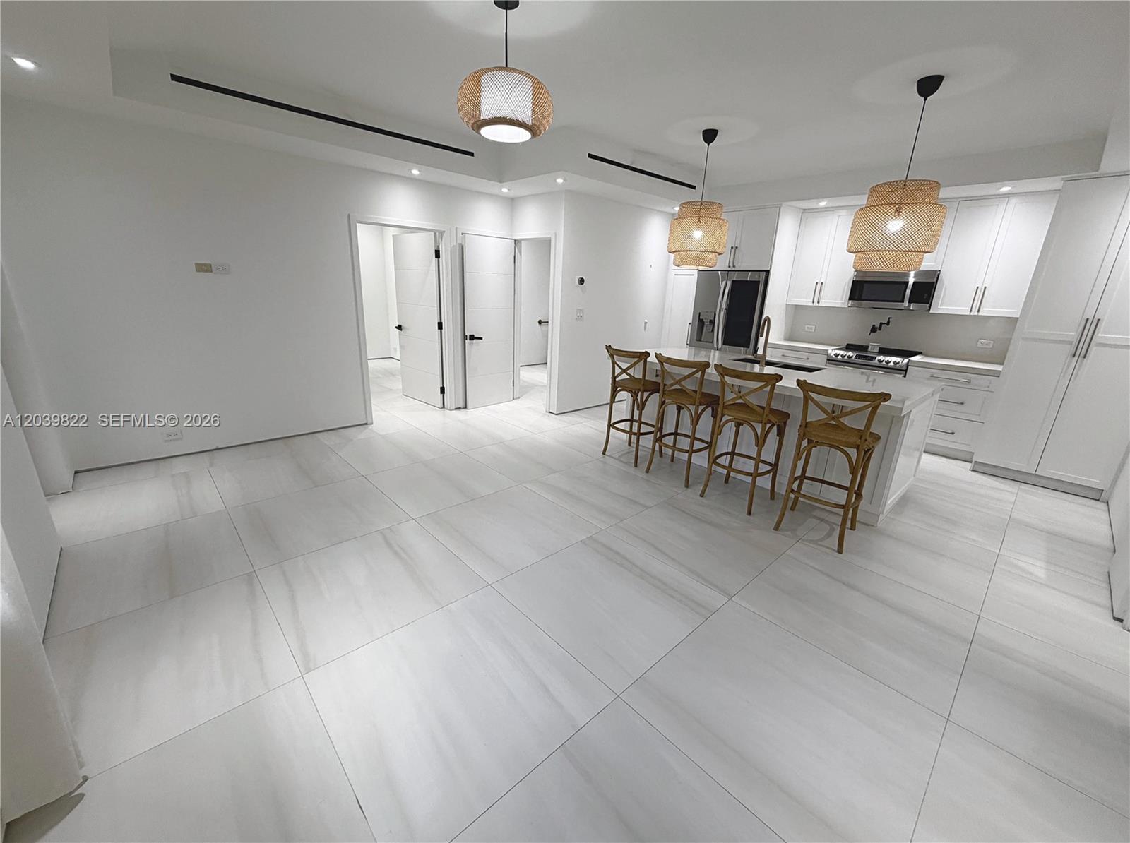 A modern kitchen features white cabinetry, a central island with four stools, and tiled flooring — 4712 SW 64th Ct, Miami FL 33155, MIAMI, FL