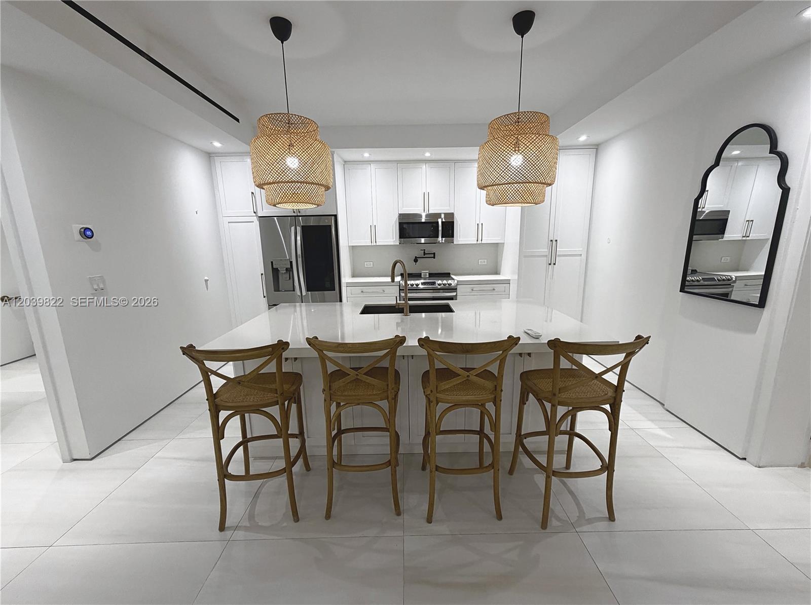 A modern white kitchen features a central island with four wooden bar stools — 4712 SW 64th Ct, Miami FL 33155, MIAMI, FL