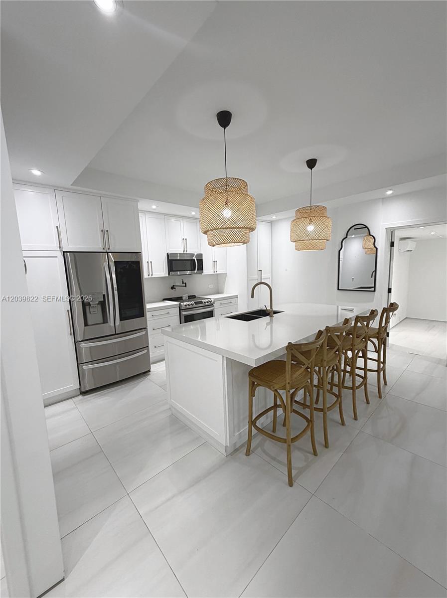 A modern white kitchen features a central island with bar stools and woven pendant lights — 4712 SW 64th Ct, Miami FL 33155, MIAMI, FL
