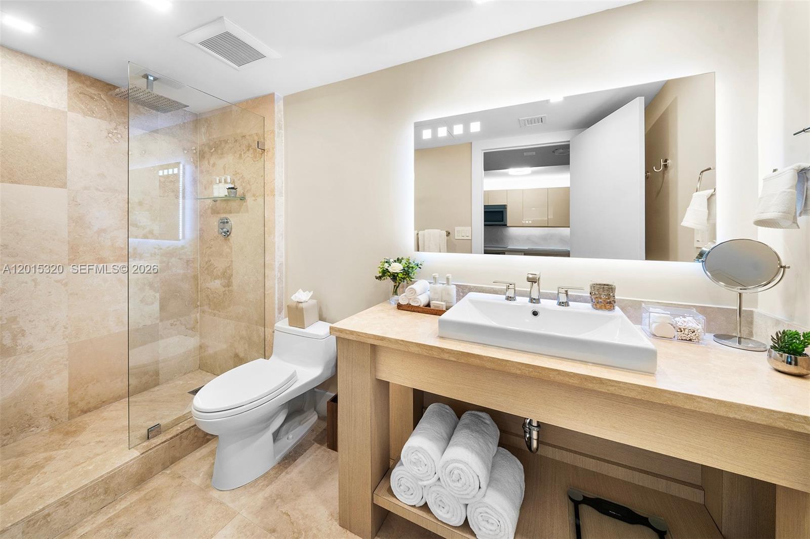 A modern bathroom features a walk-in glass shower, a wooden vanity, and a backlit mirror — 2301 Collins Ave # 1129, Miami Beach FL 33139, MIAMI BEACH, FL