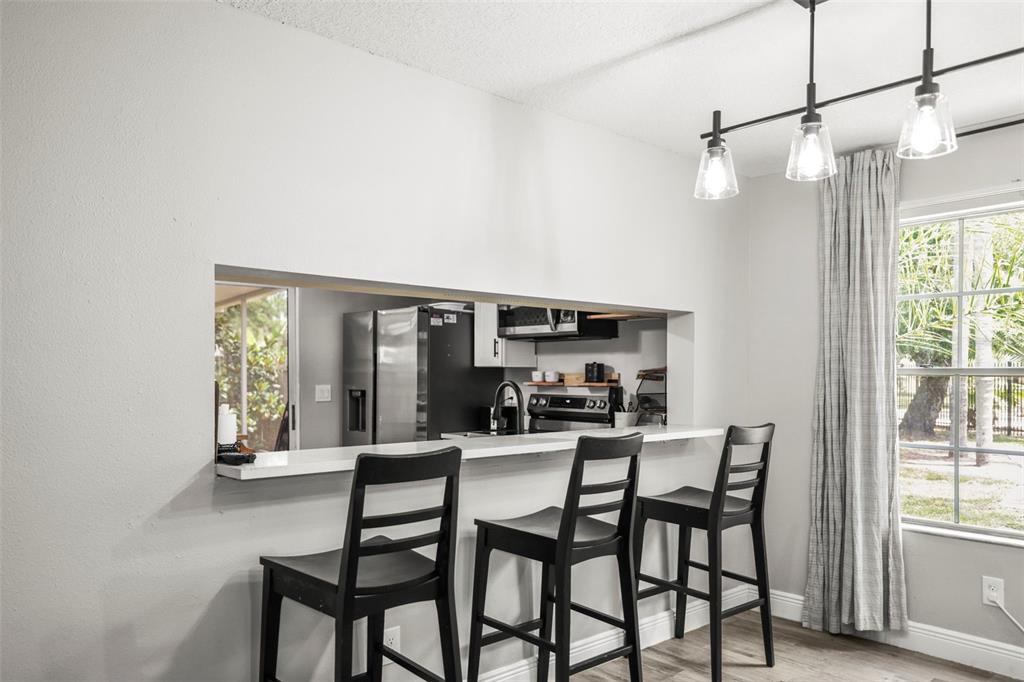 A kitchen pass-through window overlooks a dining area with three black bar stools — 933 HAMILTON COURT, PALM HARBOR, FL