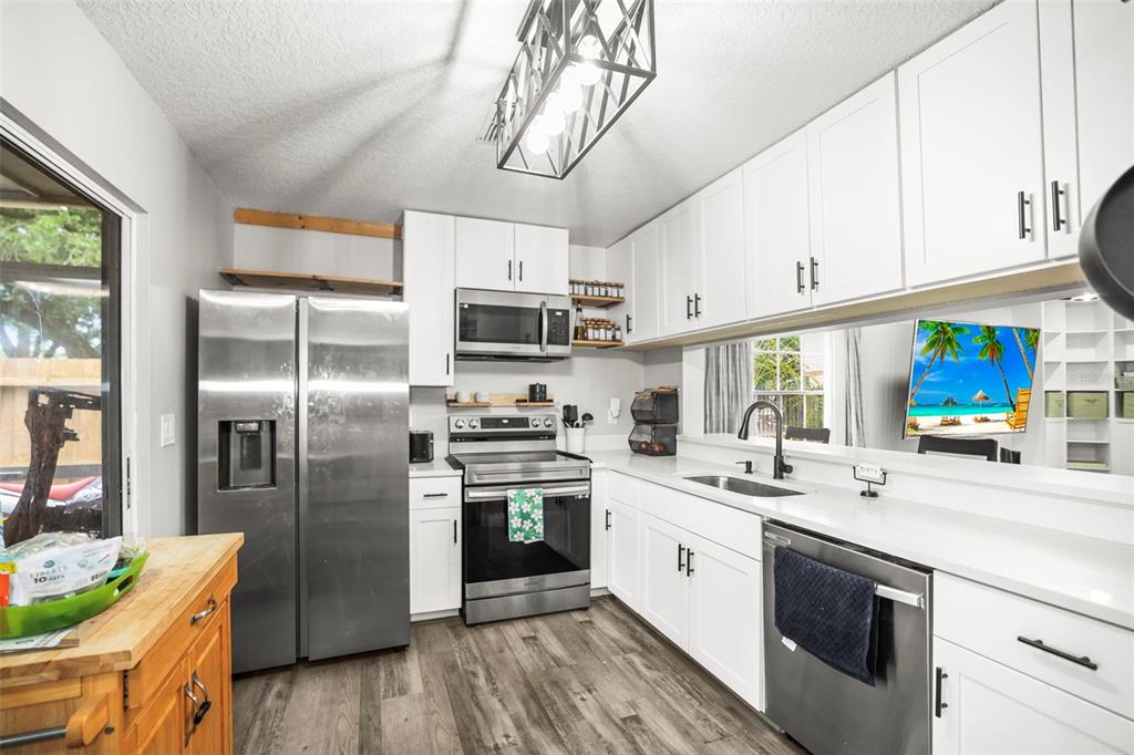 A kitchen features white cabinets, stainless steel appliances, and a pass-through window with a view — 933 HAMILTON COURT, PALM HARBOR, FL