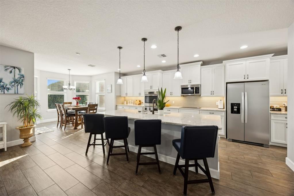 A kitchen with white cabinets, a large island with bar stools, and an adjacent dining area — 85030 Majestic Walk Boulevard, FL 32034, FL