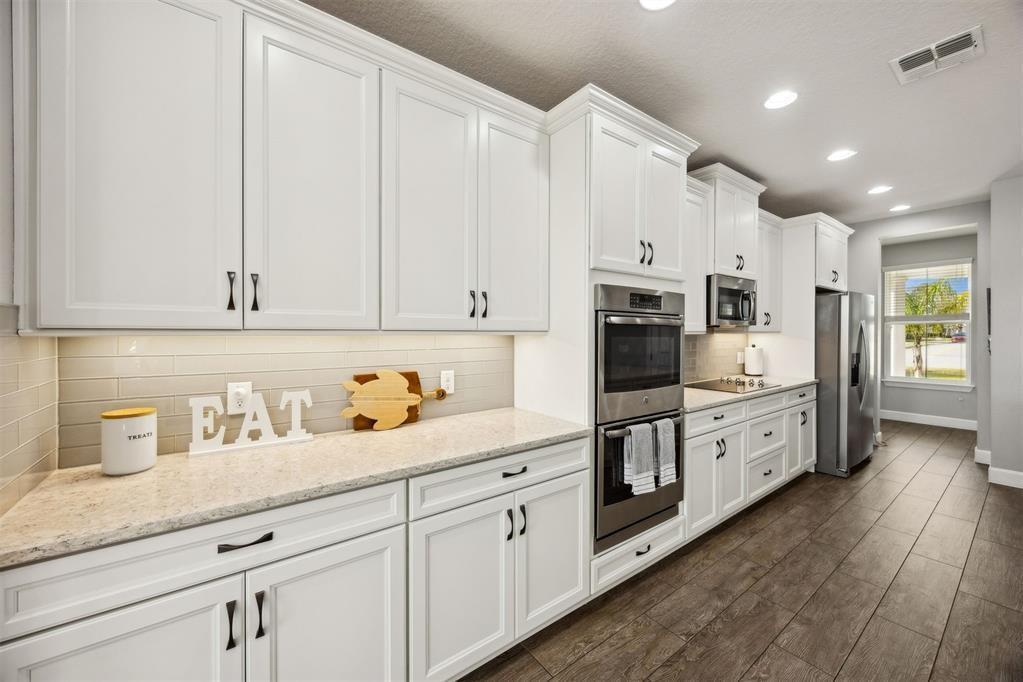 A modern kitchen features white cabinetry, stainless steel appliances, light countertops, and wood-look tile flooring — 85030 Majestic Walk Boulevard, FL 32034, FL