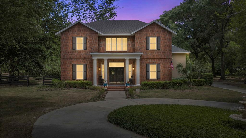A two-story brick house with a columned front porch and a circular driveway at dusk — 9175 SE 7TH AVENUE ROAD, OCALA, FL