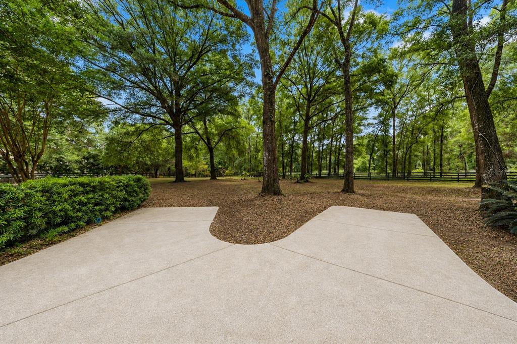A concrete patio overlooks a wooded backyard with mature trees and a black fence — 9175 SE 7TH AVENUE ROAD, OCALA, FL