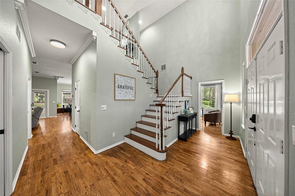 A foyer features hardwood floors, a staircase with white railings, and a high vaulted ceiling — 9175 SE 7TH AVENUE ROAD, OCALA, FL