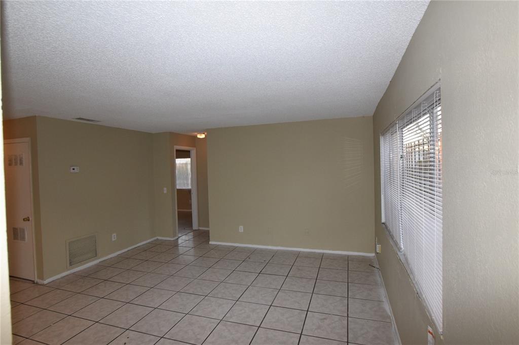 An empty room with beige walls, tiled floors, and a large window with white blinds — 3115 SPLIT WILLOW DRIVE, ORLANDO, FL