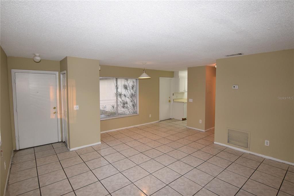 An empty room with beige walls, tiled floors, a front door, and a kitchen area — 3115 SPLIT WILLOW DRIVE, ORLANDO, FL