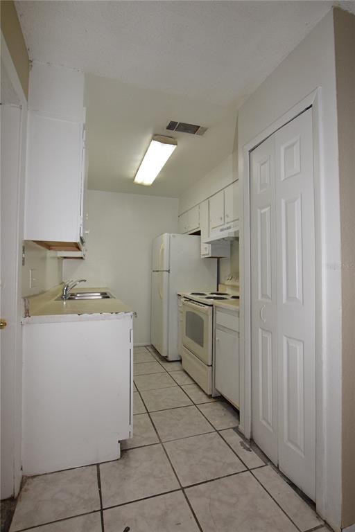 A galley kitchen features white cabinets, a white refrigerator, a stove, and tiled flooring — 3115 SPLIT WILLOW DRIVE, ORLANDO, FL