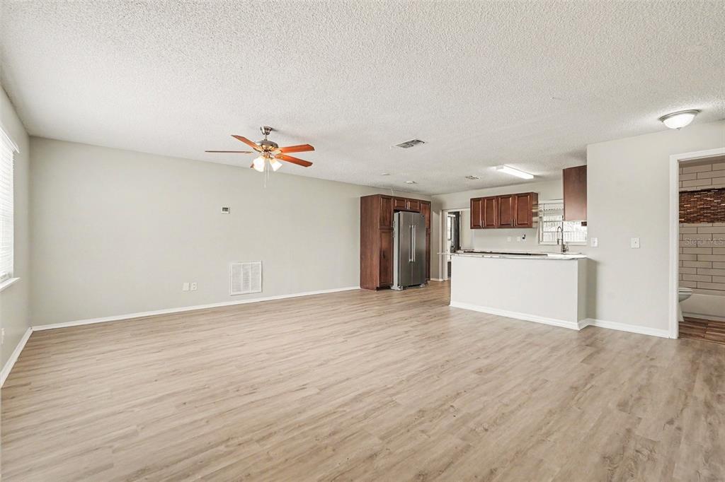 An open-concept living area features light wood-look flooring, a ceiling fan, and a kitchen — 7021 LANDOVER BOULEVARD, SPRING HILL, FL