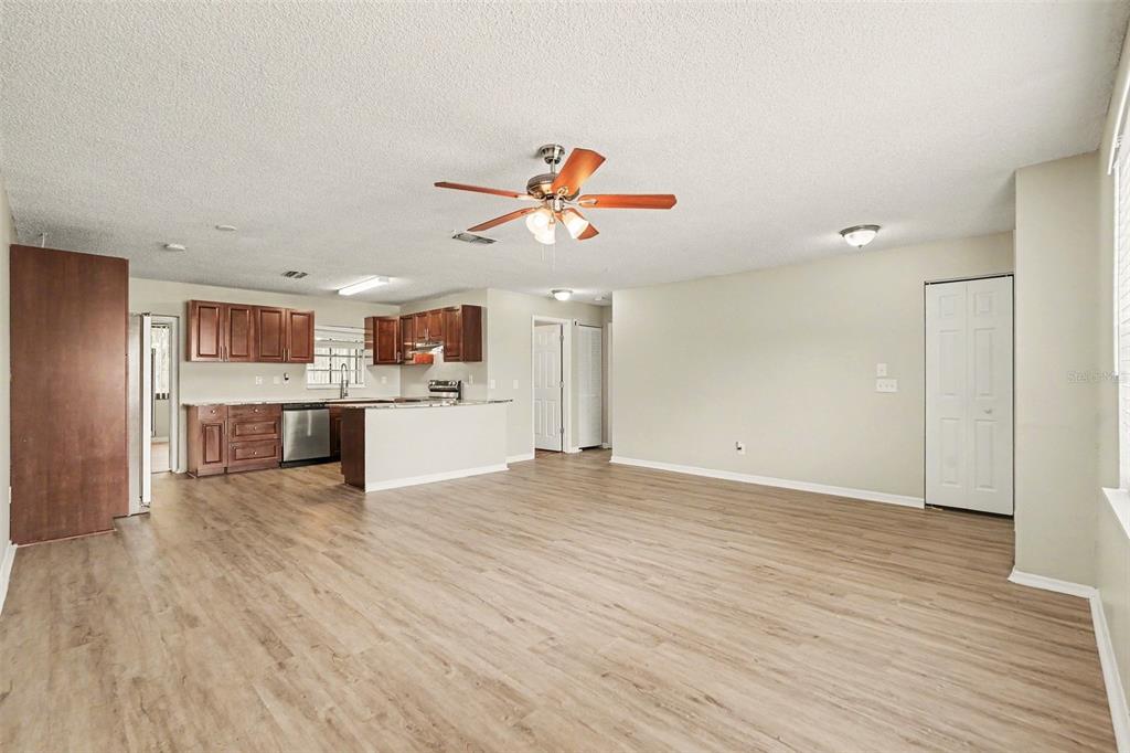 An open-concept living area features light wood-look flooring, a kitchen with brown cabinets, and a fan — 7021 LANDOVER BOULEVARD, SPRING HILL, FL