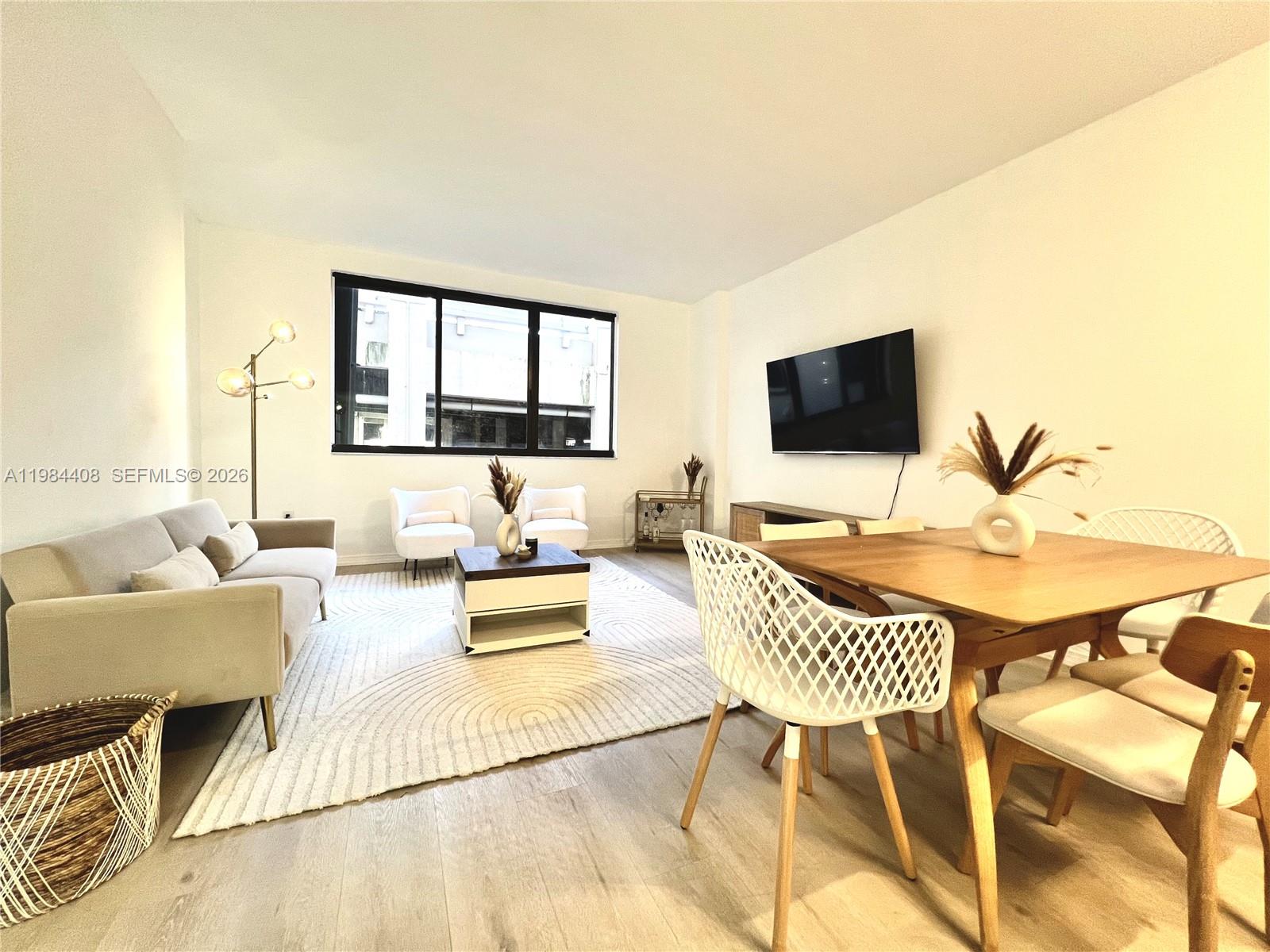A modern living and dining room features light wood floors, a neutral sofa, and a television — 540 Brickell Key Dr # 202, Miami FL 33131, MIAMI, FL