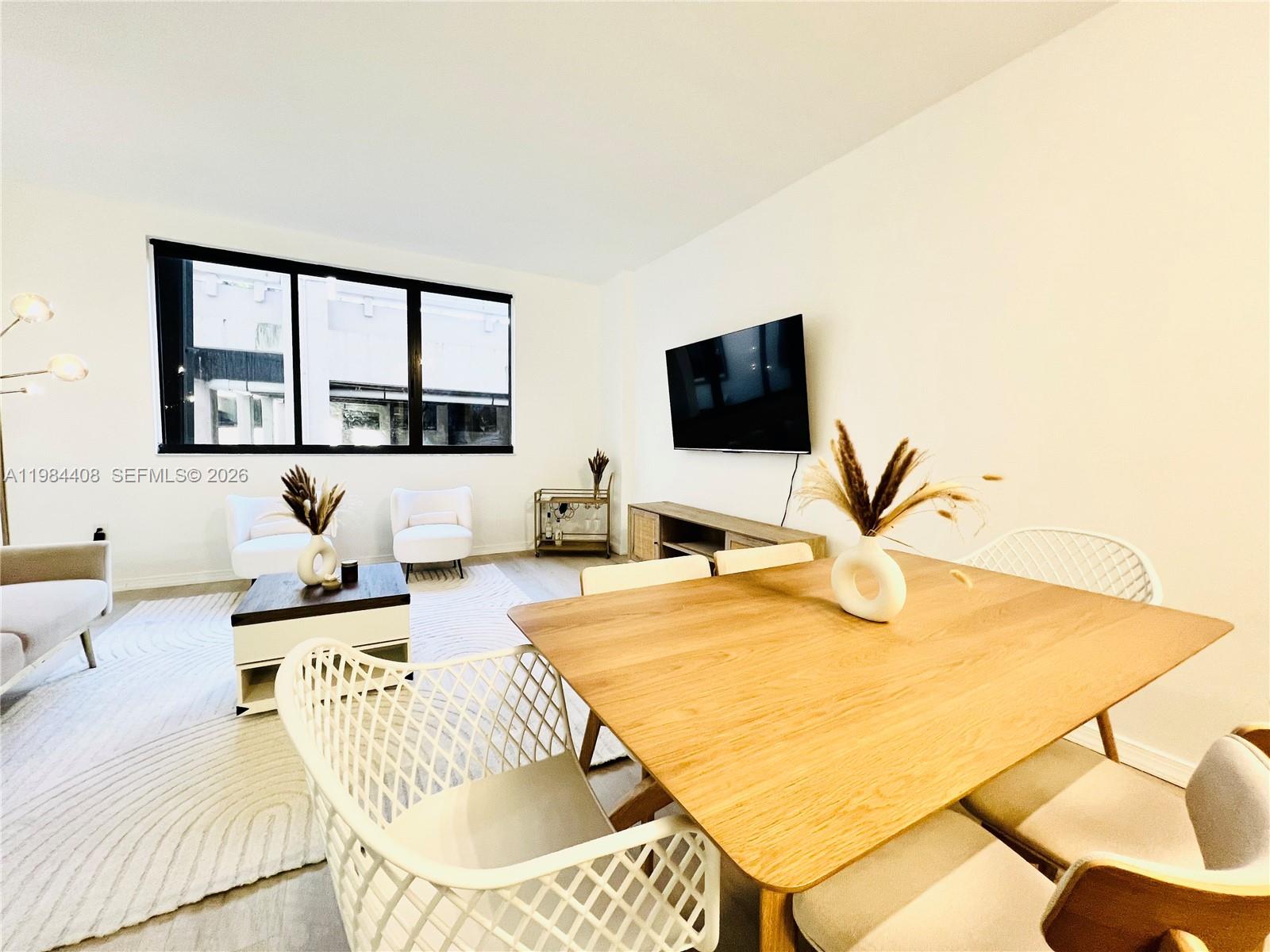 A bright living and dining area features light wood furniture, white chairs, and a television — 540 Brickell Key Dr # 202, Miami FL 33131, MIAMI, FL