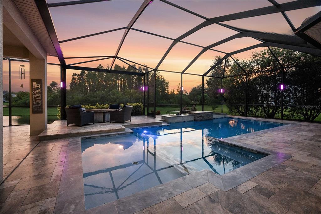 A screened-in patio features a swimming pool, hot tub, and stone pavers at sunset — 2611 COCO PALM CIRCLE, WESLEY CHAPEL, FL