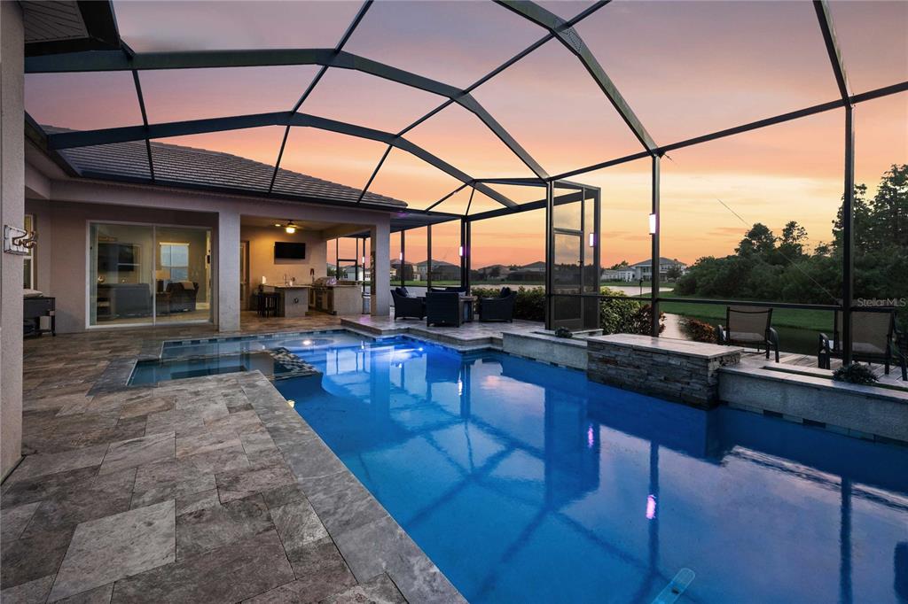 A screened-in patio features a swimming pool, spa, outdoor kitchen, and sunset lake view — 2611 COCO PALM CIRCLE, WESLEY CHAPEL, FL