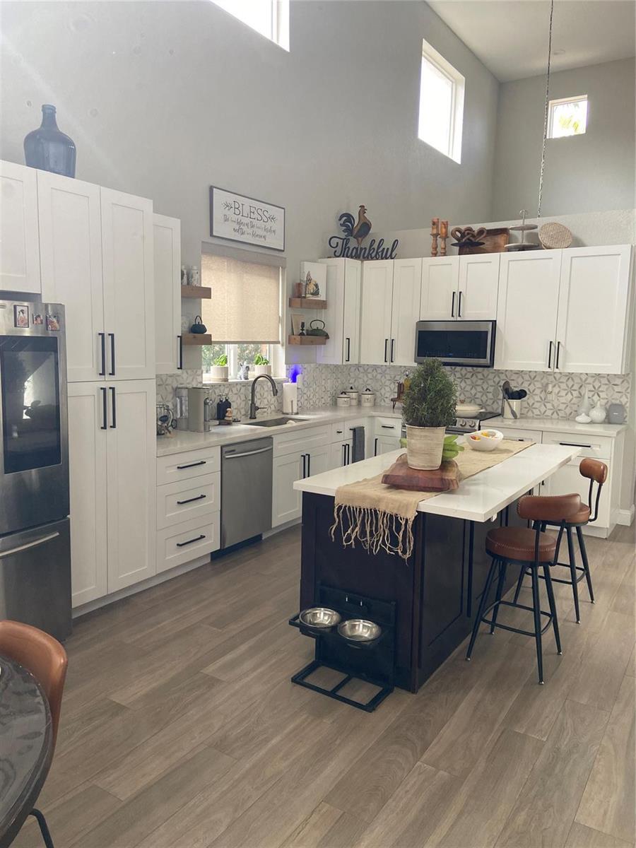 A kitchen features white cabinetry, a dark island with pet bowls, and light wood flooring — 20439 NW 9th Court, Miami FL 33169, MIAMI, FL