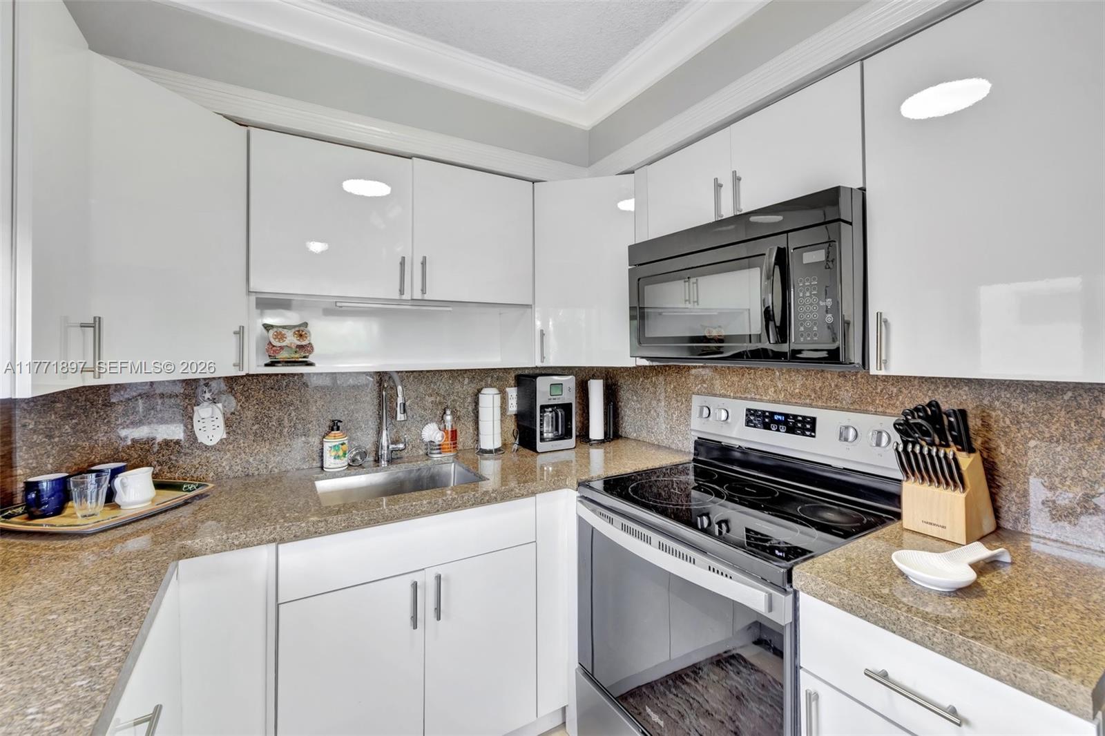 A kitchen features white cabinets, granite countertops, a stainless steel sink, and black appliances — 1012 SW 11th St # 20N, Hallandale Beach FL 33009, HALLANDALE BEACH, FL