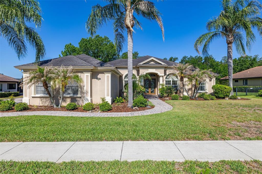 A single-story beige house with a paver walkway, palm trees, and a manicured lawn — 6535 EAGLE RIDGE WAY, LAKELAND, FL