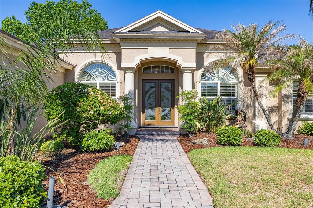 A front view of a tan house with a paved walkway and arched windows — 6535 EAGLE RIDGE WAY, LAKELAND, FL