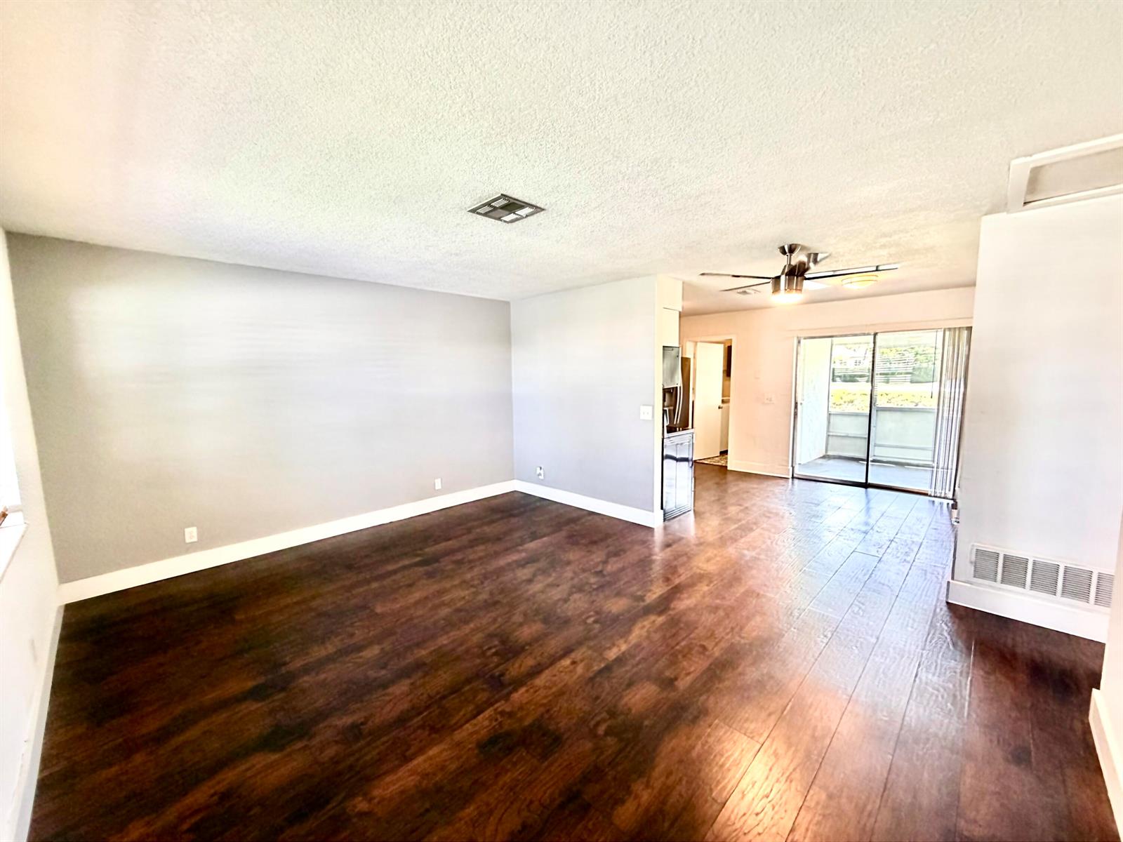 An empty living room features dark wood-look flooring, gray walls, and a sliding glass door — 2821 Duke Lane, Delray Beach FL 33445, DELRAY BEACH, FL