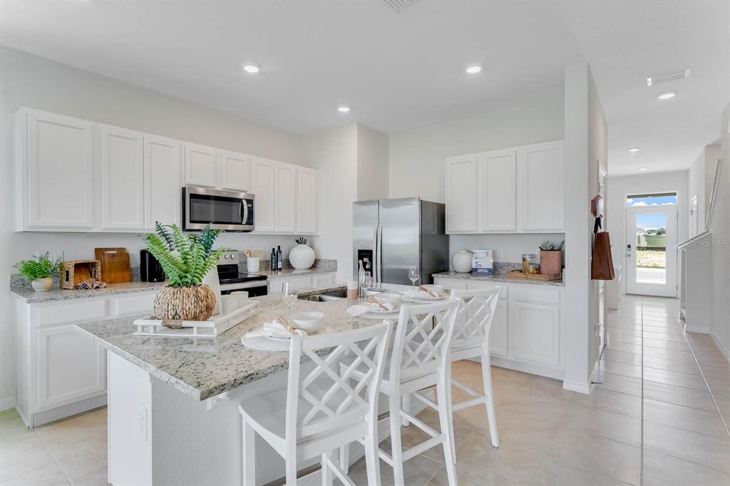 A modern kitchen features white cabinets, granite countertops, a center island, and stainless steel appliances — 2630 OLYMPIC COURT, DAVENPORT, FL