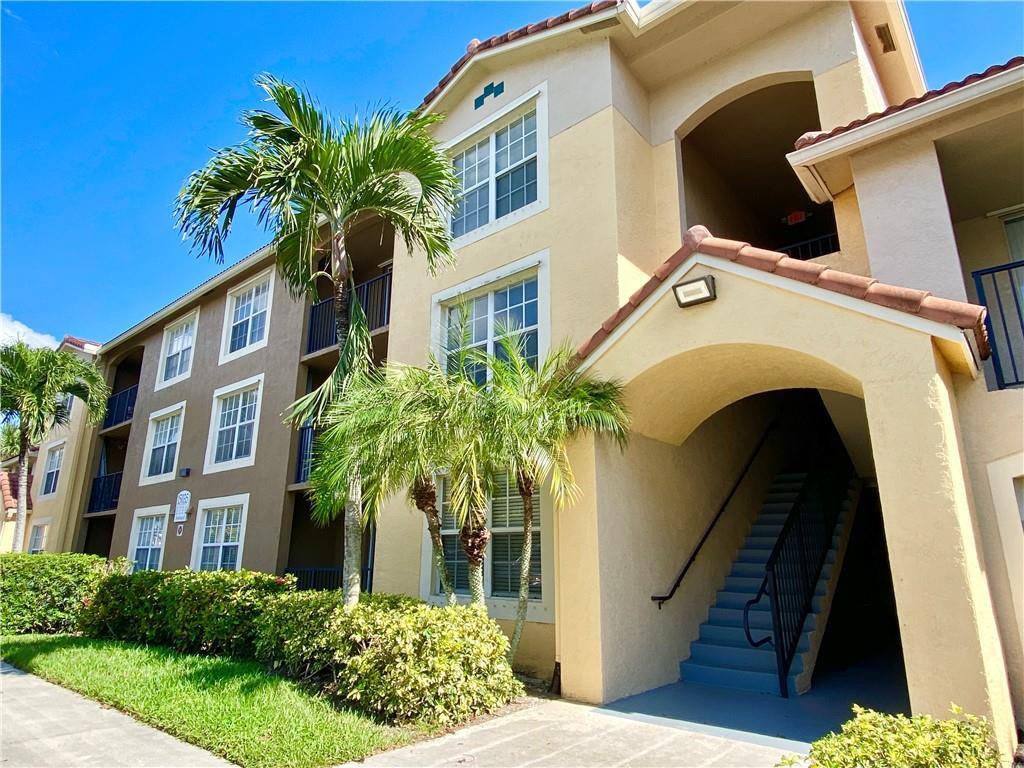 A three-story apartment building exterior features tan stucco walls, a tiled roof, and outdoor stairs — 15035 Michelangelo Boulevard # 306, Delray Beach FL 33446, DELRAY BEACH, FL